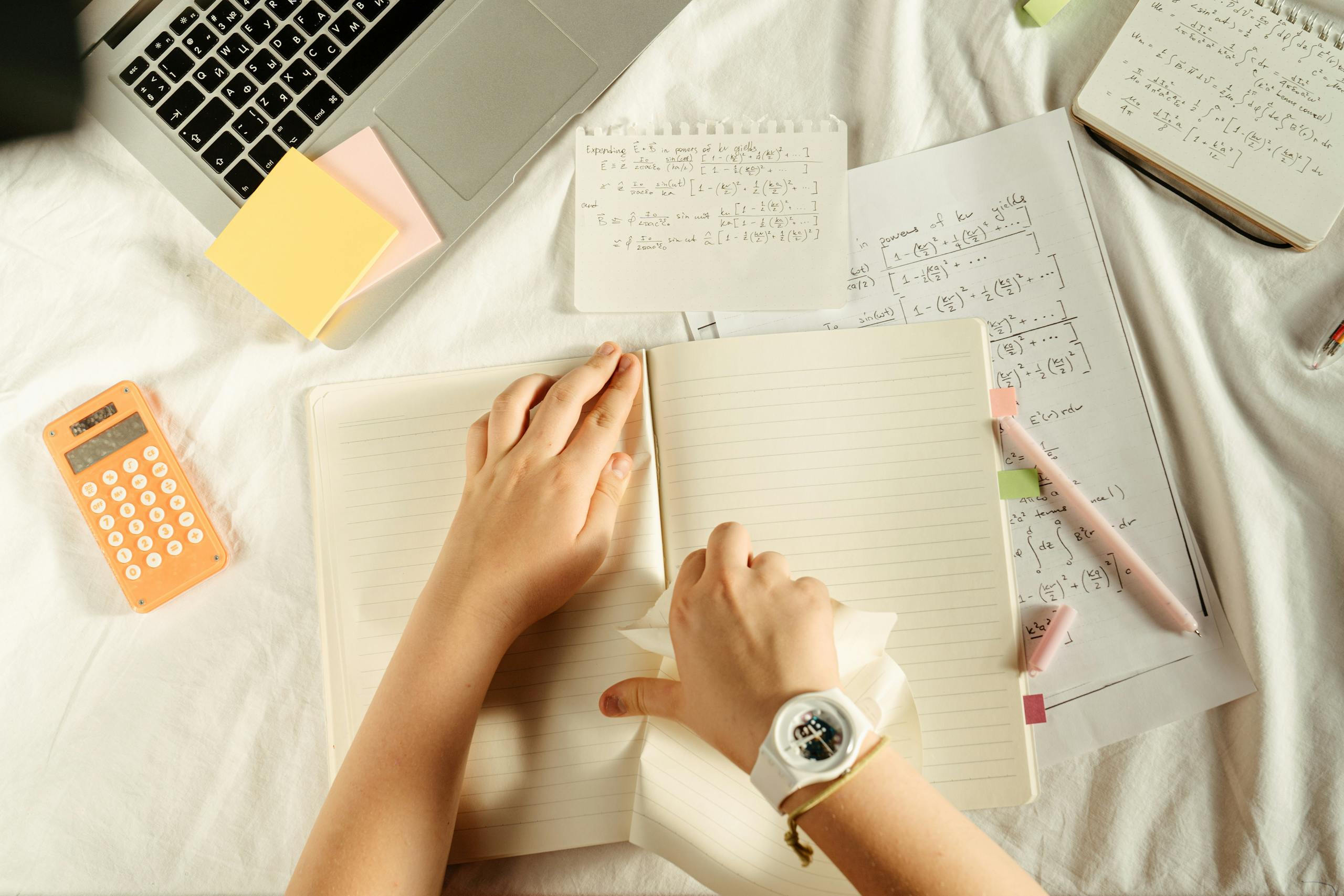 Overhead view of study materials with a laptop, calculator, and notebook on a desk.